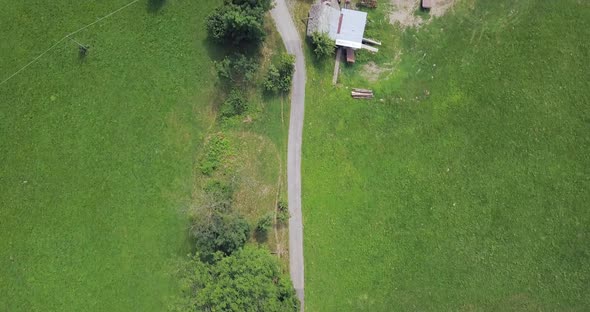 Aerial View Flying Over Road with No Car Moving Green Meadow Growing Some Trees and Farms on Both