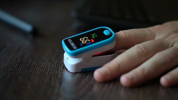 Pulse Oximeter in a Male Patient's Fingertip on Dark Wooden Table Background Medical Equipment