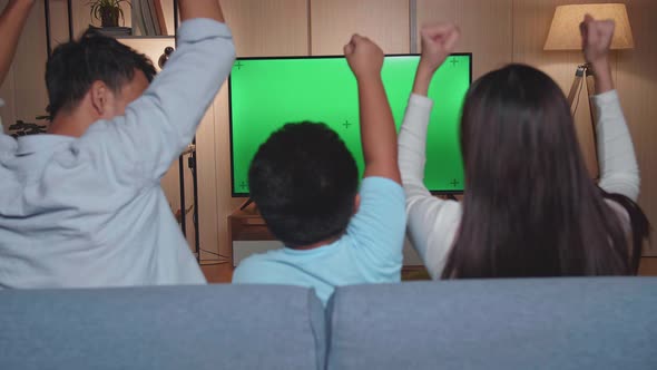 Back View Of Excited Asian Family Watching Tv With Mock Up Green Screen Together Sitting On A Sofa