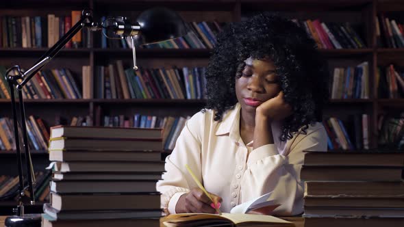 AfricanAmerican Woman Writes at Table in Semidark Room