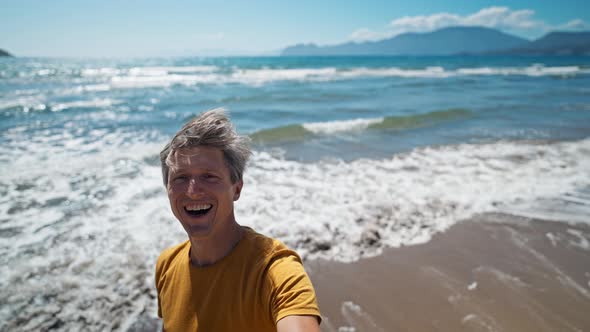 Happy Middle Aged Greyhead Man Takes Selfie at Sea Coast with Waves Enjoying Sunny Day on Beautiful