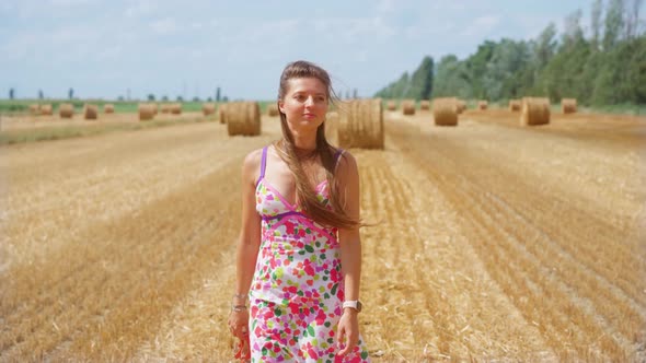 Girl Walks on the Cultivated Field with Haystacks