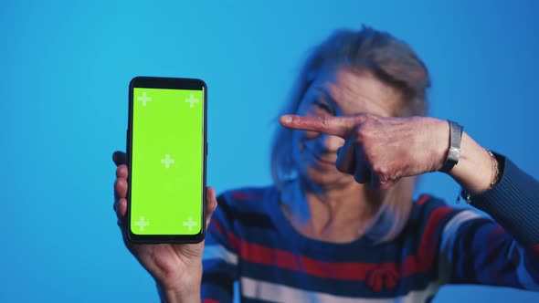 Old Woman Pointing Finger Into the Vertical Green Screen on Smartphone