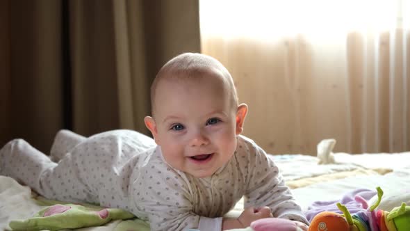 Smiling Baby Girl Learning to Crawl and Playing with Colorful Toys in White Sunny Bedroom