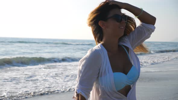 Attractive Lady in Sunglasses Smiling and Strolling Along Ocean Coast at Seascape Background