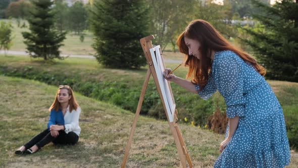 A Pretty Girl with Red Hair Draws a Portrait in Pencil, Outside in the Park.