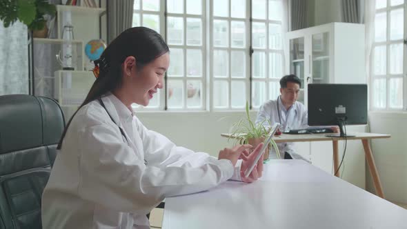 Young Asian Woman Doctor Is Using Tablet While Work With Laptop Computer In Workplace