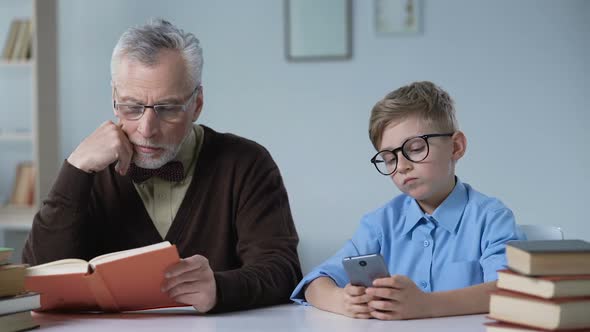 Senior Man Reading and Looking at His Grandson Playing Games on Phone, Leisure