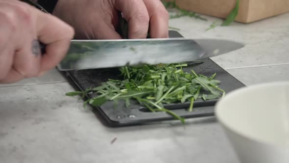 Close up camera slowly orbits chef chopping arugula on cutting board