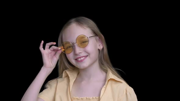 Girl in Sunglasses Smiling at Camera on Green Background