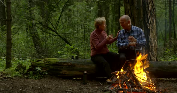 Aged Couple Hugs Sitting on Fallen Trunk at Fire in Forest