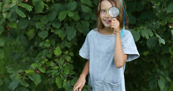 Little girl playing with a magnifying glass in her backyard make faces.