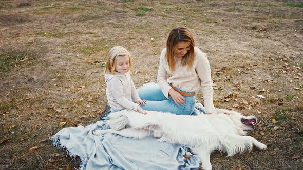 Young Mum and Her Little Child Girl Sitting on Picnic Blanket at a Glade of Autumn Park Laughing and