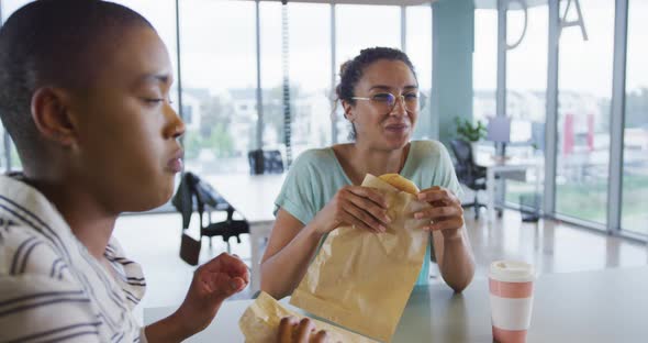 Diverse female creative colleagues eating and talking in workplace canteen