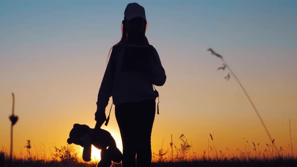 Little Girl in Dress Holding Teddy Bear Toy at Sunset. Silhouette of a Child with a Toy. Concept of