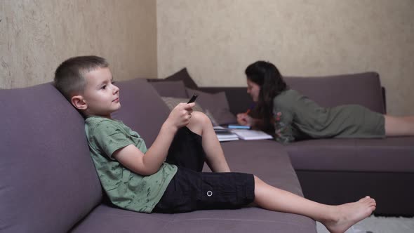 The child switches channels while sitting on the couch