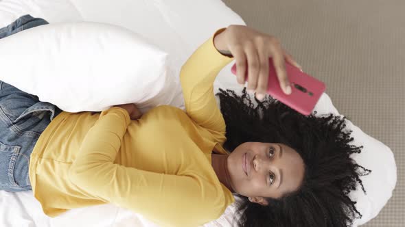 Young Cheerful African American Woman Taking Selfie Portrait with Phone on Bed