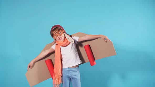 Joyful Kid Wearing Plane on Back Isolated Over Blue Background