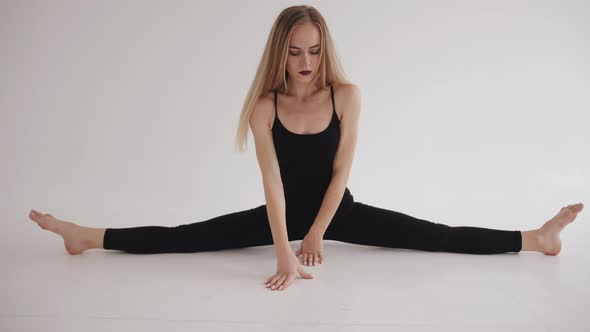 A Graceful Young Girl Sits Down on a Transverse Twine and Lies on the Floor in a White Studio