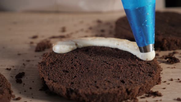 Pastry Chef Is Pouring Cream with Pastry Bag on Chocolate Sponge Cake. Making Cake in Bakery