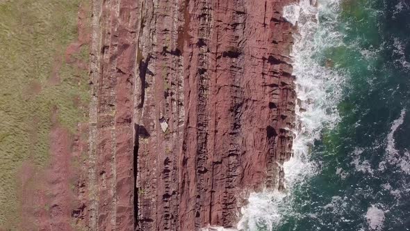 Drone overhead ariel footage of red cliffs and crashing waves