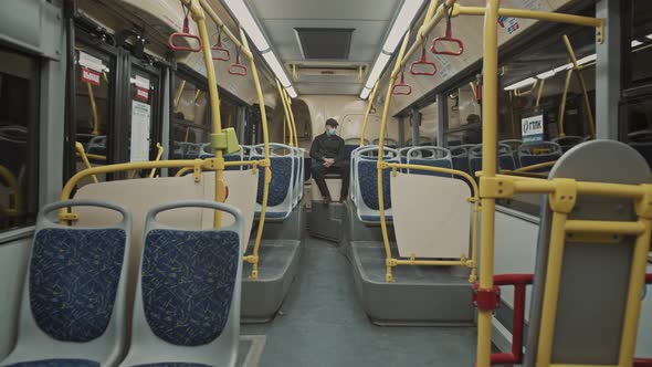 A Young Man Wearing a Protective Medical Mask Sits on an Empty Bus