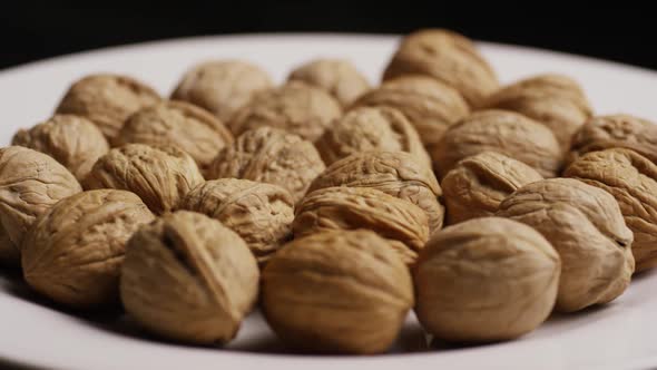 Cinematic, rotating shot of walnuts in their shells on a white surface