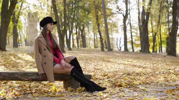 Glamorous Girl in Stylish Clothes Sits on Bench in a Pose in the Autumn Park
