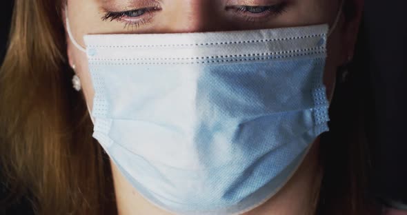 Young Woman in a Medical Mask Looks at the Camera on a Black Background