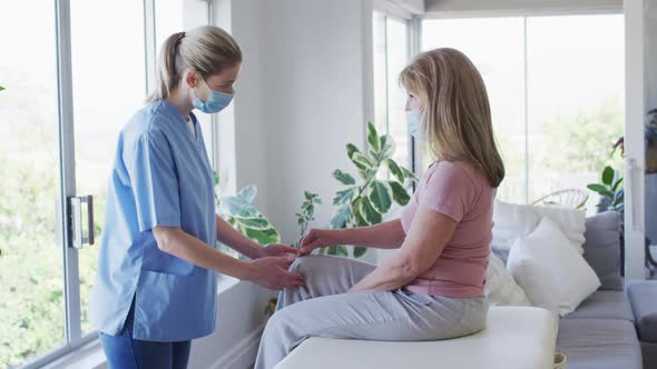 Female health worker stretching knee of senior woman at home