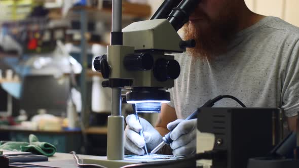 Repairman Looks Through Microscope Produces Solders on Circuit Board of Device.