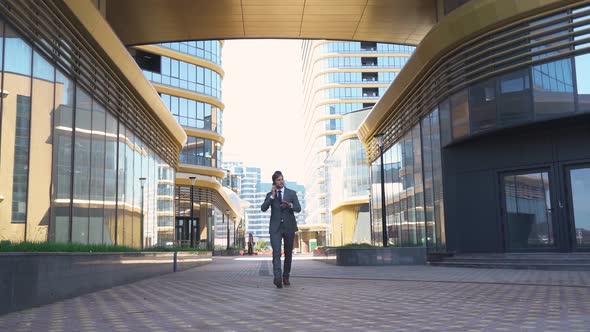 Young Businessman in a Suit Walking Next To the Glass Skyscraper and Talking on a Mobile Phone, Top