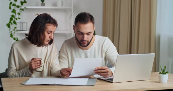 Focused Millennial Caucasian Couple Calculating Domestic Paper Bills at Home Using Laptop Paying