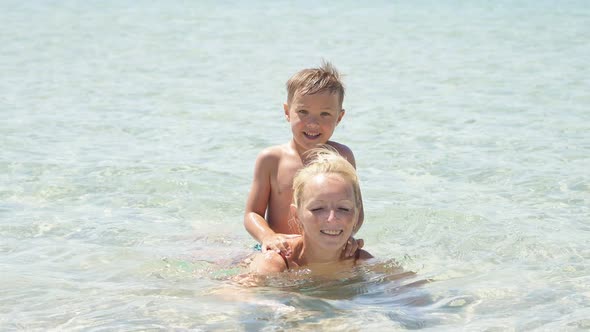 Child with His Mother Swims in the Crystal Clear Sea Near the Shore and Learns To Swim