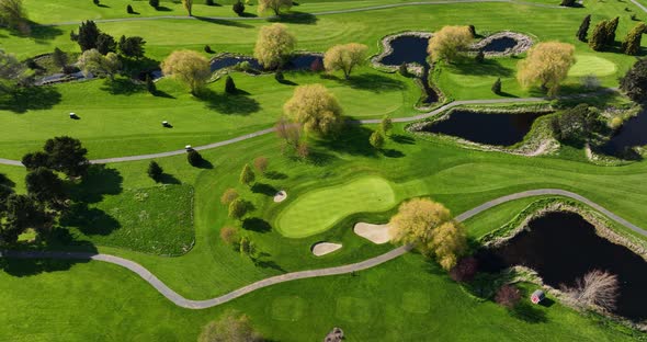Top down aerial shot of golf carts driving through a green and lush golf course.