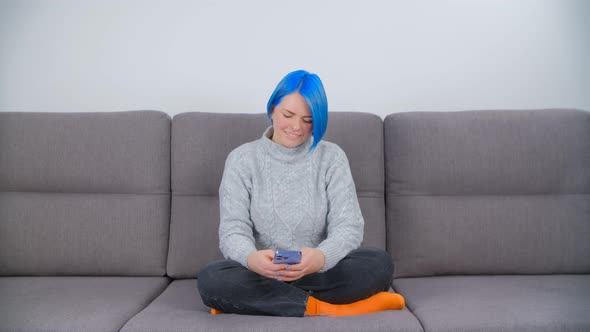 Millenial girl with colored blue hair using mobile phone for communication and entertainment online