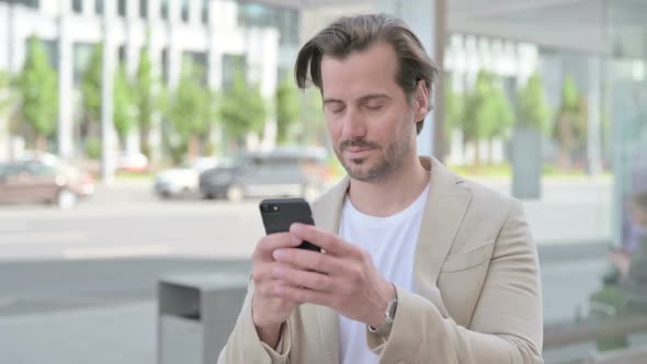Young Man Browsing Internet on Smartphone Outdoor