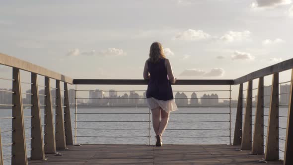 Young European Woman is Standing By the Railing at the Wooden Pier and Enjoying the View of the Lake