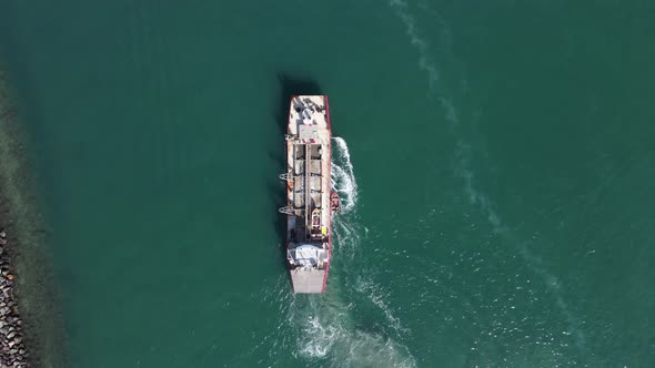 A small pilot boat maneuvers docks on a large industrial dredging vessel as it navigates through the