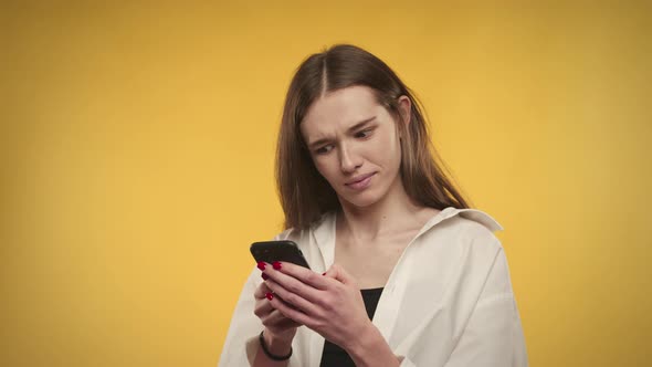 Young Adult Caucasian Woman Texting on Her Smartphone on a Bright Yellow Background