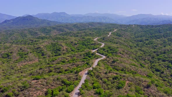 Cinematic drone flight over road surrounded by green planted landscape and mountain range in backgro