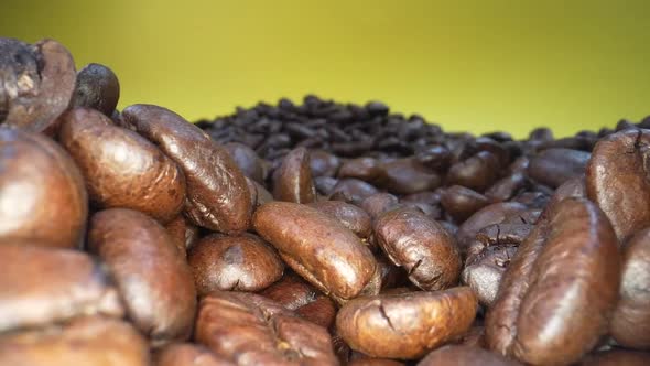 Slow zoom out shot of roasted coffee beans falling down in slow motion in front of yellow background