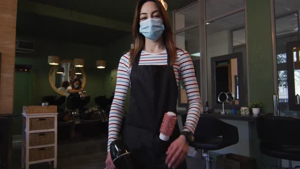 Portrait of female hairdresser wearing face mask holding hair dryer at hair salon