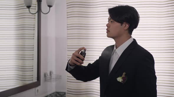 Side View of Young Asian Man in Wedding Suit Spraying Perfume in Slow Motion Smelling Fragrance