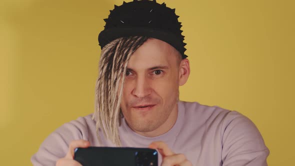 Young handsome man in black cap taking pictures on mobile phone on yellow background.