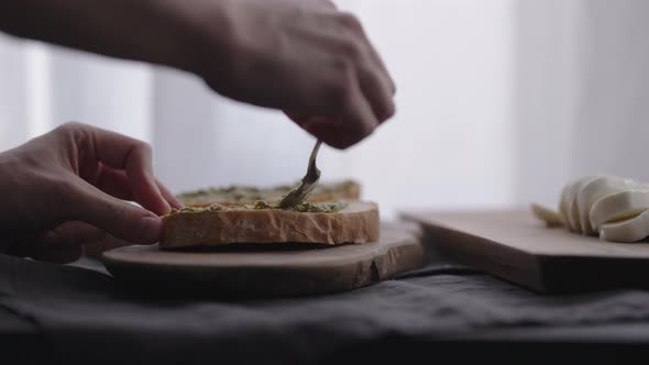 Slow Motion Man Making Ciabatta Bruschettas with Mozzarella and Pesto on Olive Board with Window on