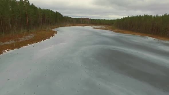 Drone flies over a frozen lake in winter in Estonia surrounded by forest