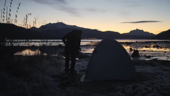 Man Setting Up Tent Close To River In Winter