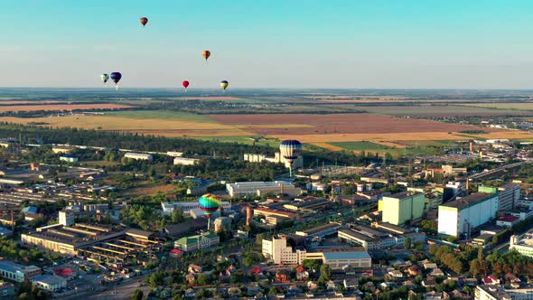 Multicolored balloons fly over fields, houses, trees. Blue sky.