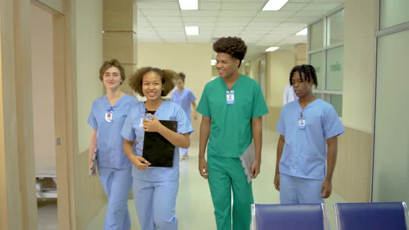 Four members of male and female doctors walking in hospital corridor talking, medical health 